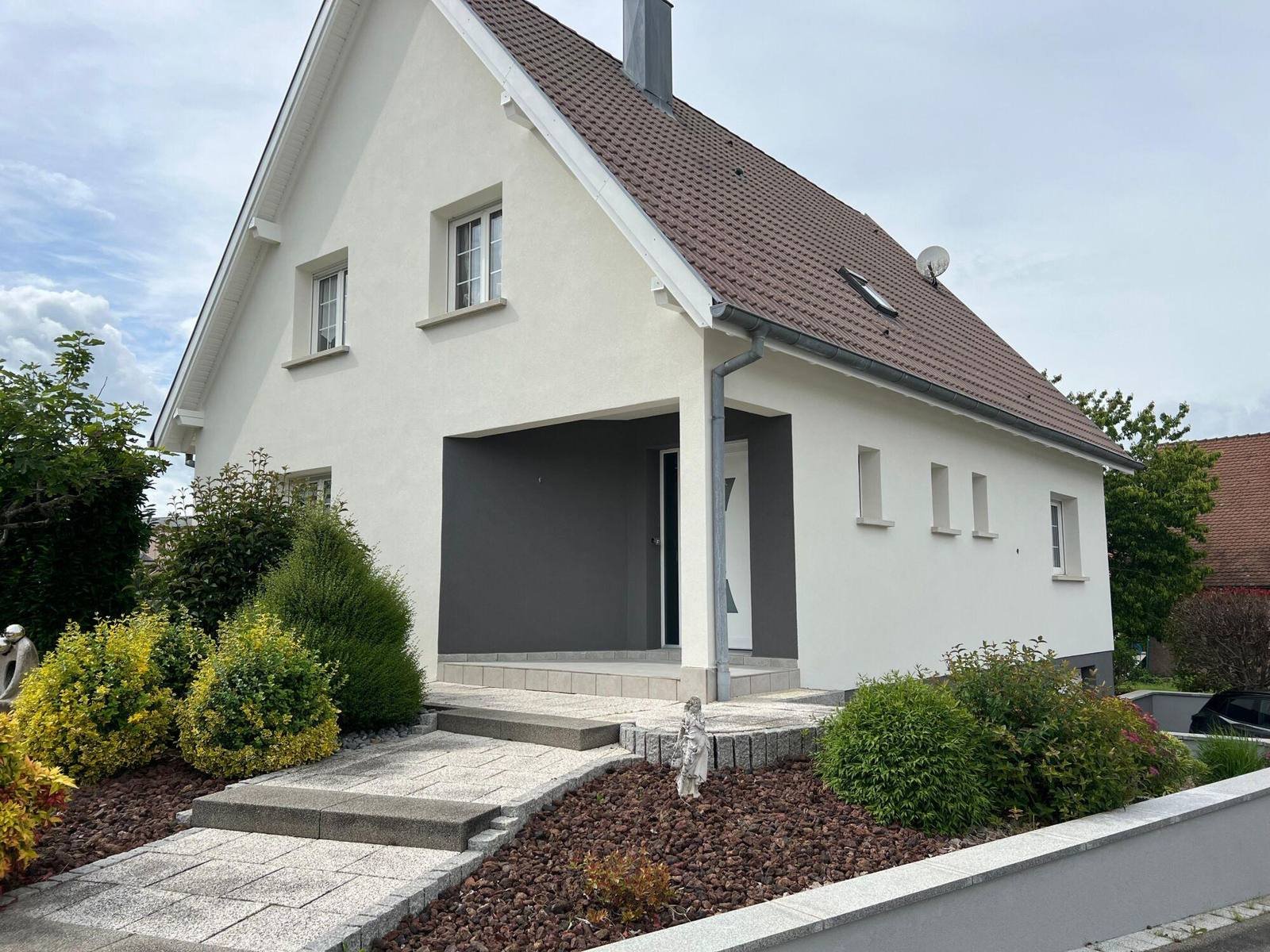 Pavillon à la façade enduite blanche, toit en tuiles sombres et jardin